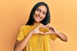 © Krakenimages.com - Young brunette woman wearing yellow tshirt over yellow background smiling in love doing heart symbol shape with hands. romantic concept.