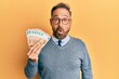 © Krakenimages.com - Handsome middle age man holding bunch of 50 euro banknotes scared and amazed with open mouth for surprise, disbelief face