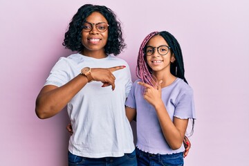 Poster - Beautiful african american mother and daughter wearing casual clothes and glasses cheerful with a smile on face pointing with hand and finger up to the side with happy and natural expression