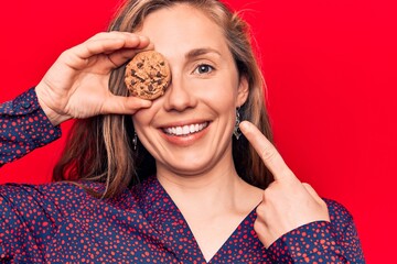 Canvas Print - Young beautiful blonde woman holding chocolate chips cookie smiling happy pointing with hand and finger