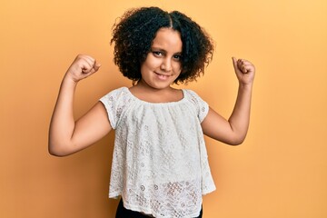 Poster - Young little girl with afro hair wearing casual clothes showing arms muscles smiling proud. fitness concept.