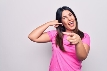 Wall Mural - Young beautiful brunette woman wearing casual pink t-shirt standing over white background smiling doing talking on the telephone gesture and pointing to you. Call me.