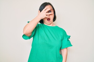 Poster - Brunette woman with down syndrome wearing casual clothes and glasses peeking in shock covering face and eyes with hand, looking through fingers afraid