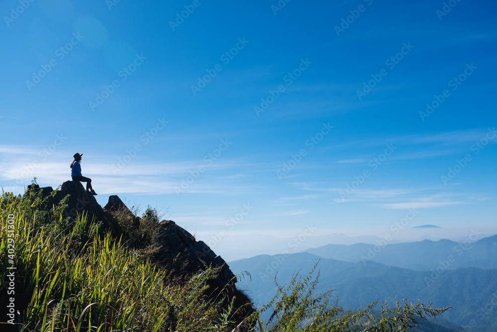 A female traveler hiking and sitting on mountain peak, looking at a beautiful view - obrazy, fototapety, plakaty 