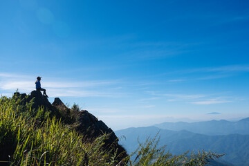 a female traveler hiking and sitting on mountain peak, looking at a beautiful view