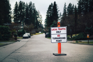 Local traffic only, no turnaround point. Traffic road sign for streets plagued with traffic not from the area. Defocused and desaturated residential neighborhood and tall pine trees.