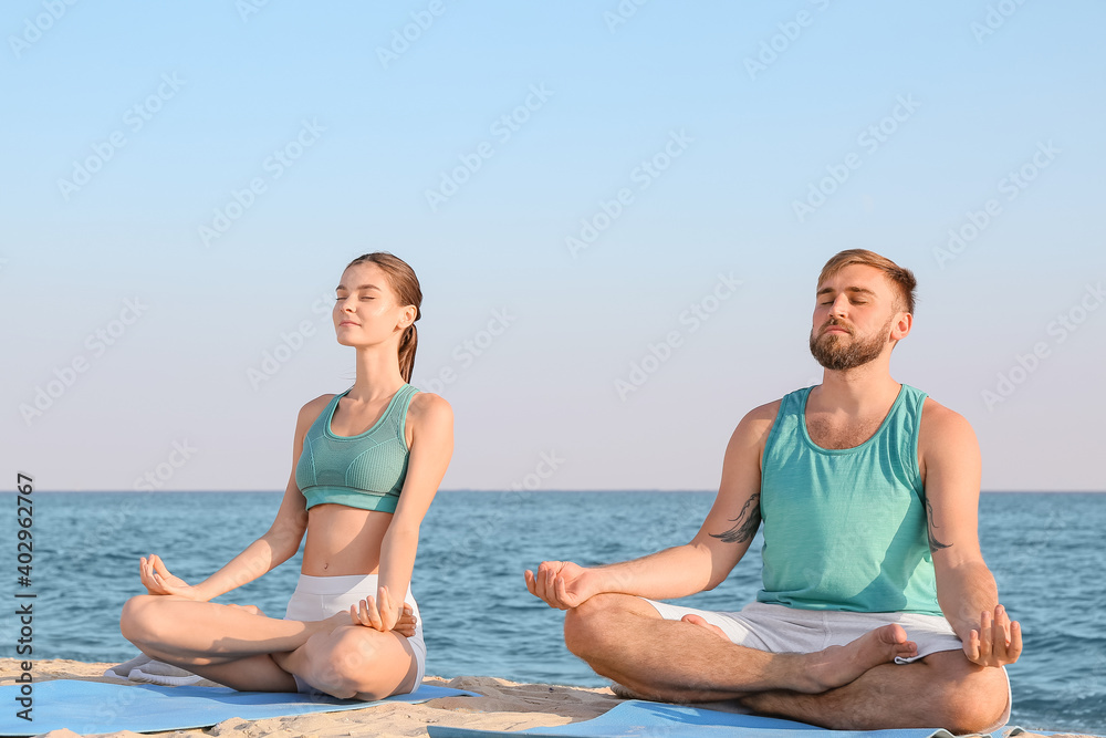 Sporty young couple practicing yoga on sea beach