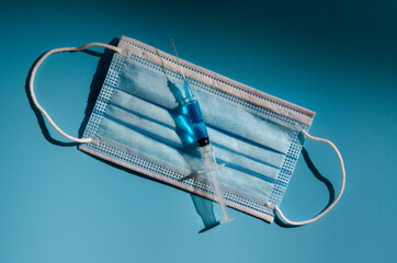 Syringe with coronavirus vaccine in medicine mask on blue background, medicine and drug