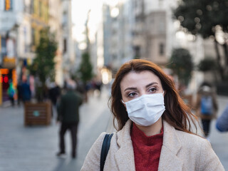 Beautiful girl wearing protective medical mask and fashionable clothes stands at street. New normal lifestyle concept.