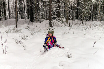 Happy positive girl sits on the snow for a walk in the forest outside the city.