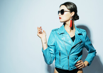 Wall Mural - Stylish brunette model posing in fashionable look. Blue leather jacket, black swimsuit, sunglasses and red earrings. Fashion concept.