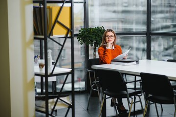 Young businesswoman sitting at workplace and reading paper in office