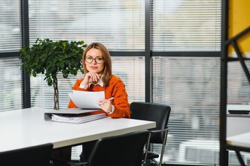 Young businesswoman sitting at workplace and reading paper in office