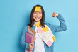 © wayhome.studio  - Positive office worker raises arm and shows muscles feels strong poses with paper documents smiles happily wears casual sweater has reminder sticker stuck on forehead isolated over blue background