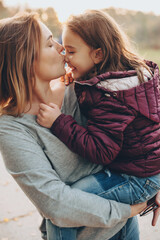 careful mother kissing her daughter and holding her outside in a sunny day