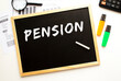© Ihar - Text PENSION written in chalk on a slate board. Office desk with office supplies.