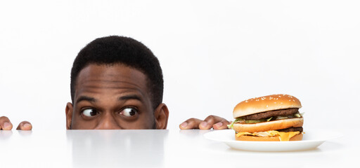 Wall Mural - Hungry African Guy Looking At Burger On Desk In Studio