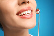 © New Africa - Young woman with mouth mirror on blue background, closeup. Cosmetic dentistry