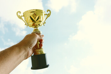 Wall Mural - Man holding up a trophy cup as a winner against the blue sky. Award and victory concept