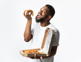 Wall Mural - Hungry African Guy Eating Slice Of Pizza Posing In Studio