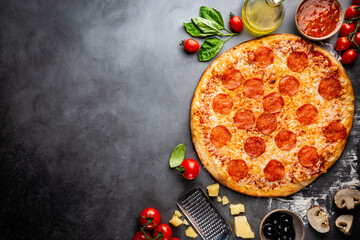 Poster - Tasty pepperoni pizza and cooking ingredients tomatoes basil on black concrete background. Top view of hot pepperoni pizza. Banner