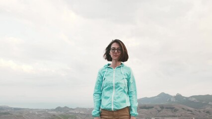 Wall Mural - Beautiful traveler young woman wearing in blue jacket posing high over mountain valley in autumn.