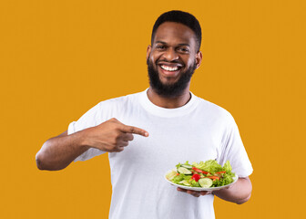 Wall Mural - African Man Pointing Finger At Salad Standing On Yellow Background