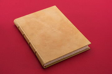 Fototapete - Antique book with light brown leather hardcover on cardinal red background