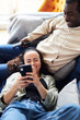 © Southworks - Overhead Shot Of Relaxed Young Couple At Home On Sofa Watching TV And Checking Mobile Phone