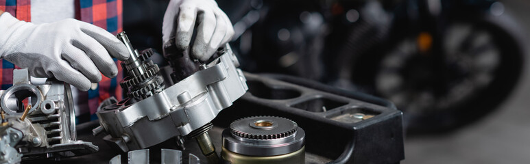 cropped view of mechanic in gloves checking disassembled motorcycle gearbox, banner