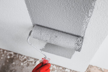 The painter paints the outer wall of the building with a gray paint roller - facade work - painting the plaster