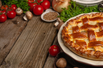 Appetizing ruddy meat pie on wooden table with variety of ingredients background. Backstage of preparing tasty homemade meal. Recipe book or culinary site. Space for text.