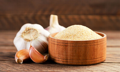 Ground garlic in a plate and cloves on a wooden background