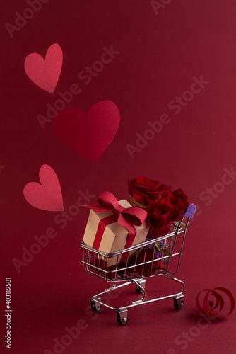 St. Valentine\'s Festive sale concept with gift box rose, and red paper hearts in the shopping cart against a red background.
