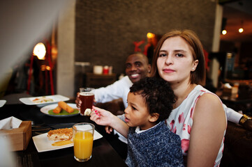 Happy multiethnic family with boy kid spend time at restaurant. Relationships of african man and white european woman.