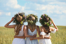 Young Women Wearing Wreaths Made Of Beautiful Flowers In Field On Sunny Day, Back View
