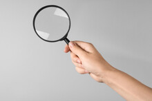 Woman Holding Magnifying Glass On Grey Background, Closeup. Find Keywords Concept