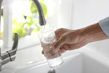 Wall Mural - Man pouring water into glass in kitchen, closeup