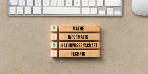 Germany acronym MINT and explanation MATHEMATICS, TECHNOLOGY, SCIENCE and ENGINEERING on wooden cubes with computer keyboard on paper background