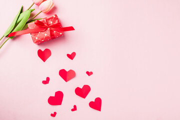 Valentines' day background. Red gift box with ribbon bow, wood red hearts shaped and flower composition greeting card for love isolated on pink background with copy space. Top View from above