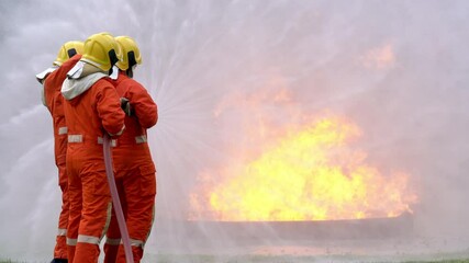 Wall Mural - Firefighter teamwork in fire protection suit on safety rescue duty spray water from fire hose extinguishing crackle fire flames inside danger burning premises. Fireman fighting a fire in training area