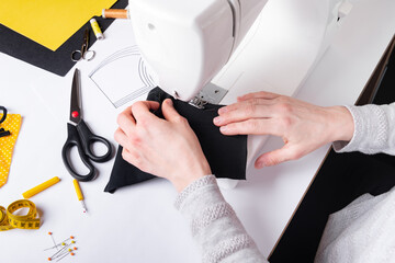 Wall Mural - Woman hands using a sewing machine to sew a black face mask during the coronavirus pandemia. Domestic sewing due to the shortage of medical materials.