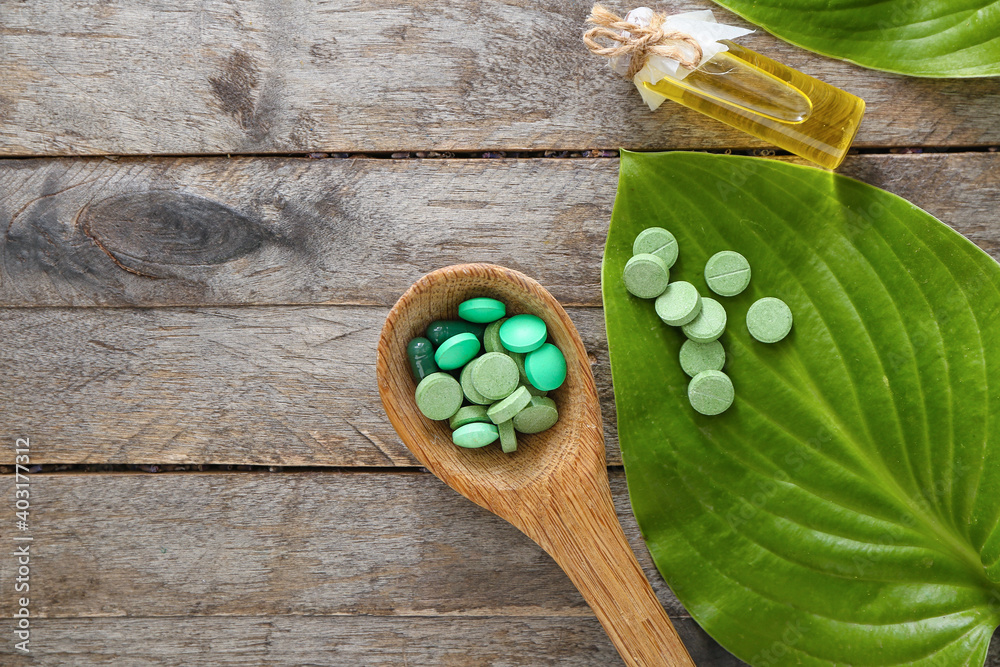 Spoon with plant based pills on wooden background