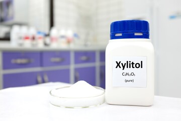 Sticker - Selective focus of a bottle of pure xylitol sugar substitute with powder in petri dish. White laboratory background with copy space.	