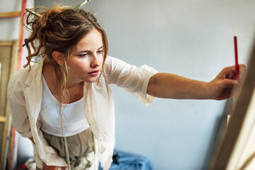 Wall Mural - Girl artist sitting on the floor in the art studio and painting on paper with a brush. A woman painter with glasses painting and searching for imagination in the workshop.