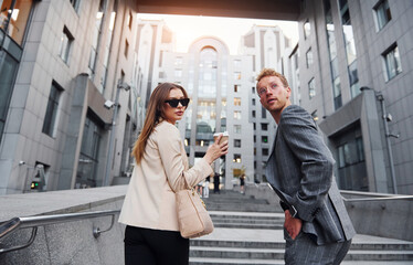 Wall Mural - Girl holds drink. Woman and man in the town at daytime. Well dressed people