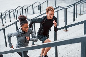 Running on bleachers. European man and african american woman in sportive clothes have workout together