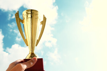 Wall Mural - man holding up a trophy cup as a winner against the blue sky. award and victory concept
