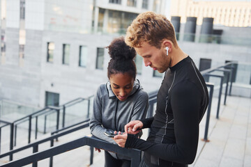 Wall Mural - Using phone. European man and african american woman in sportive clothes have workout together