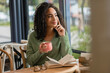 © LIGHTFIELD STUDIOS - dreamy african american woman holding cup of coffee and looking away near book on table